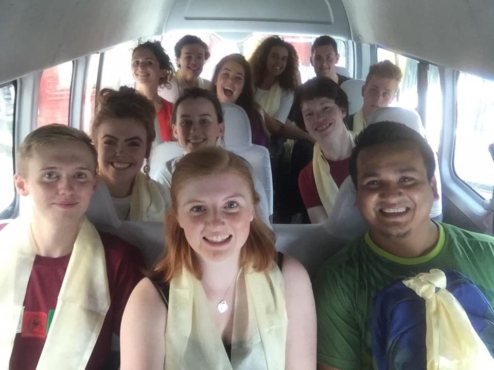 A group of cheerful people posing for a selfie in a vehicle, wearing neck sashes.